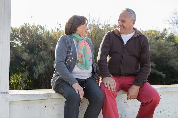 Pareja jubilada sentada y riendo al aire libre