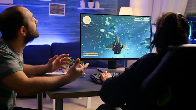 Pareja de jugadores haciendo gesto de ganador mientras juegan campeonato virtual de tirador espacial