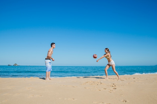 Pareja jugando al voleibol de playa por la orilla