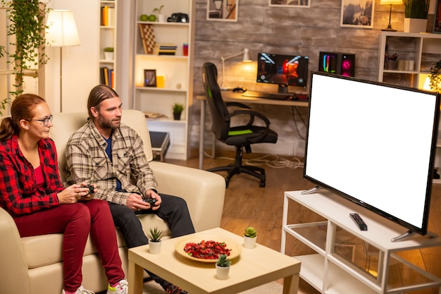 Pareja jugando videojuegos en la pantalla de TV en blanco aislado a altas horas de la noche en la sala de estar