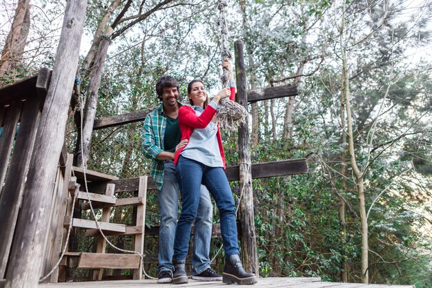 Pareja juguetona sosteniendo la cuerda en el parque de aventura