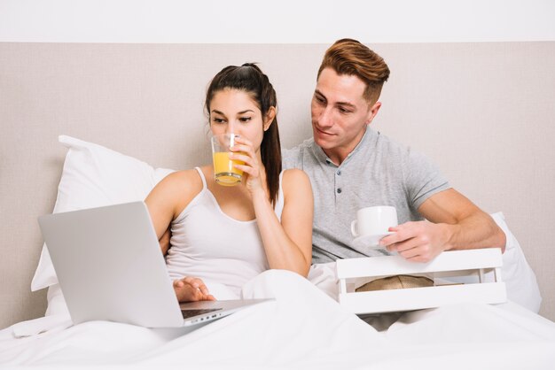 Pareja con laptop desayunando en la cama