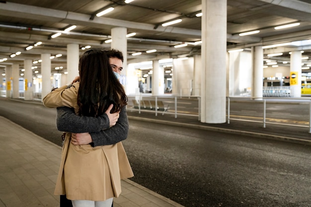 Pareja de larga distancia de tiro medio abrazándose en el aeropuerto