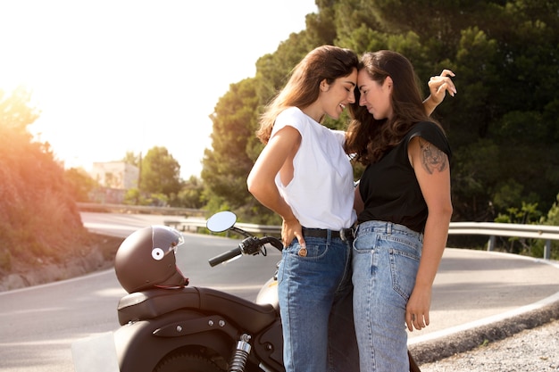 Pareja de lesbianas abrazando cerca de la motocicleta durante un viaje por carretera