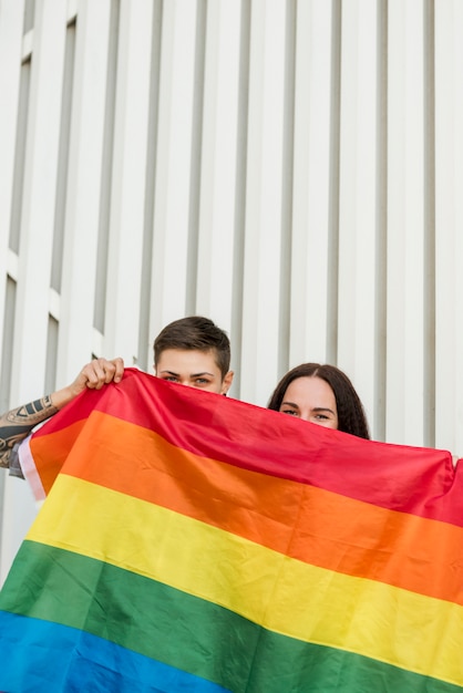 Foto gratuita pareja de lesbianas se esconde detrás de la bandera lgbt