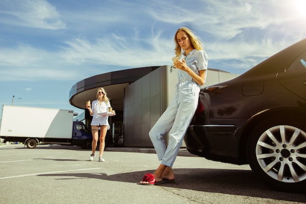 Pareja de lesbianas jóvenes preparándose para el viaje de vacaciones en el coche en un día soleado. Ir de compras y tomar café antes de ir al mar o al océano. Concepto de relación, amor, verano, fin de semana, luna de miel.