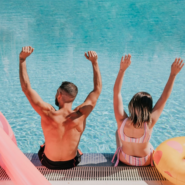 Foto gratuita pareja levantando brazos al lado de piscina