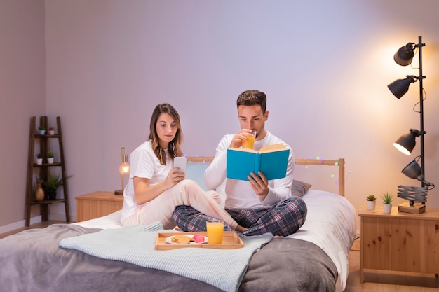 Pareja leyendo un libro y desayunando en la cama