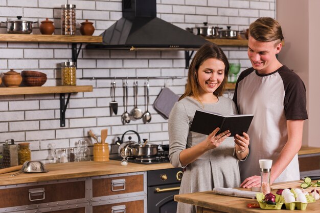 Pareja leyendo libro de recetas mientras cocinan juntos