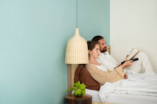 Pareja leyendo un libro y viendo la televisión en su habitación durante las vacaciones