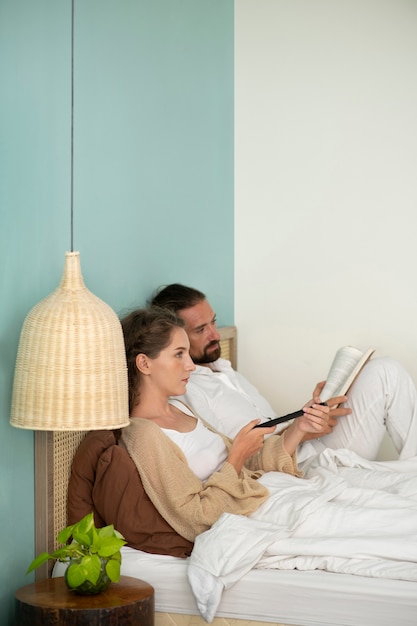 Foto gratuita pareja leyendo un libro y viendo la televisión en su habitación durante las vacaciones