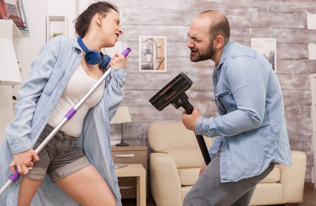 Pareja limpiando la casa y cantando en la aspiradora