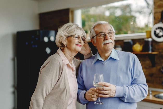 Foto gratuita pareja madura pensativa sonriendo mientras está de pie en la cocina y soñando despierto