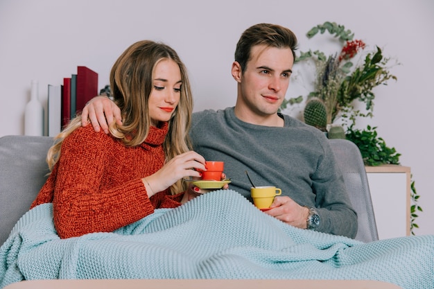 Foto gratuita pareja bajo manta cálida bebiendo bebidas calientes