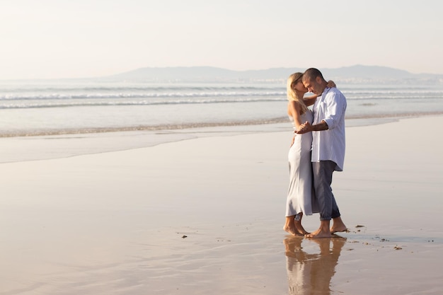 Pareja masculina y femenina activa pasando tiempo en la playa. Marido y mujer con ropa informal abrazándose y bailando el día de verano. Vacaciones, felicidad, concepto de relación.