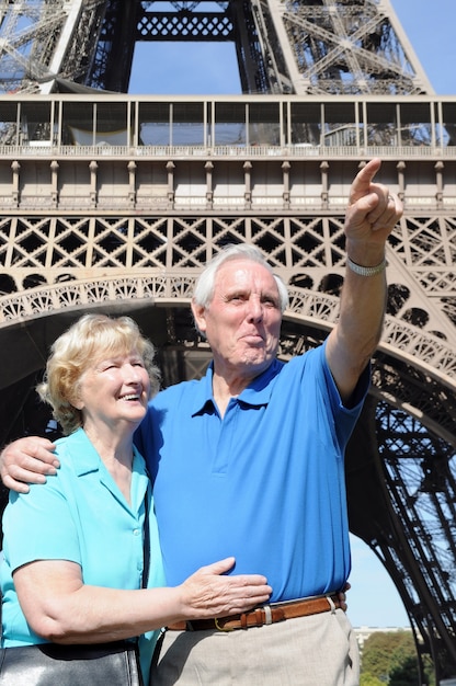 Pareja mayor apuntando hacia algo delante de la torre eiffel en parís