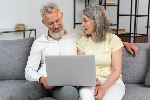 Pareja mayor, en casa, en el sofá, usar la computadora portátil