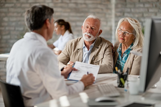 Pareja mayor consultando con un trabajador de la salud sobre su póliza de seguro mientras tiene una reunión en la clínica