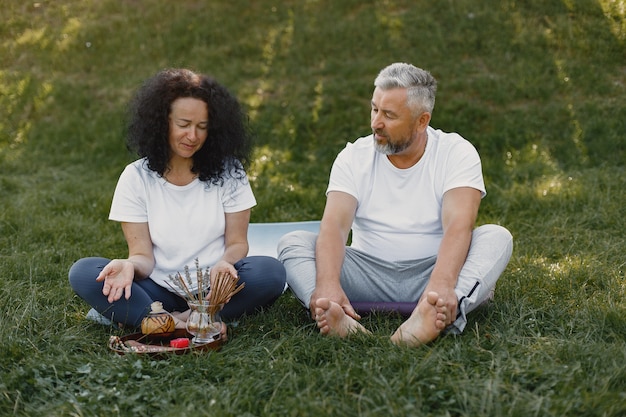 La pareja mayor está haciendo yoga al aire libre. Estirarse en el parque durante el amanecer. Morena con camiseta blanca.