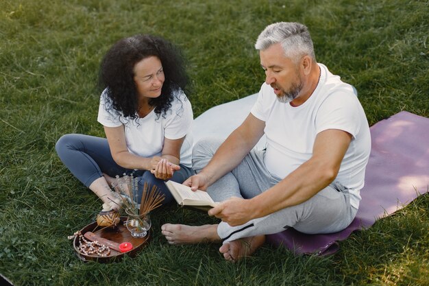 La pareja mayor está haciendo yoga al aire libre. Estirarse en el parque durante el amanecer. Morena con camiseta blanca.