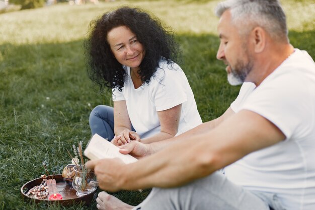 La pareja mayor está haciendo yoga al aire libre. Estirarse en el parque durante el amanecer. Morena con camiseta blanca.