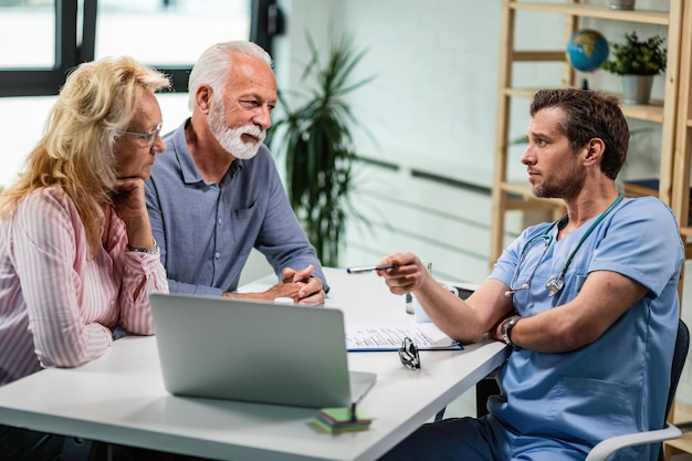 Pareja mayor hablando con su médico mientras les muestra algo en una computadora