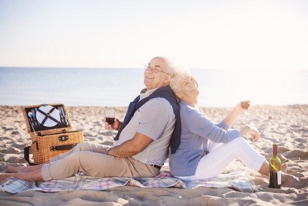 Pareja mayor, relajante, con, un, botella de vino, en la playa