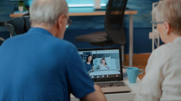 Pareja mayor reunida con familiares en videollamada en línea. Pensionistas hablando con la familia en el hospital en un chat de teleconferencia remota, usando una computadora portátil. Internet de telecomunicaciones.