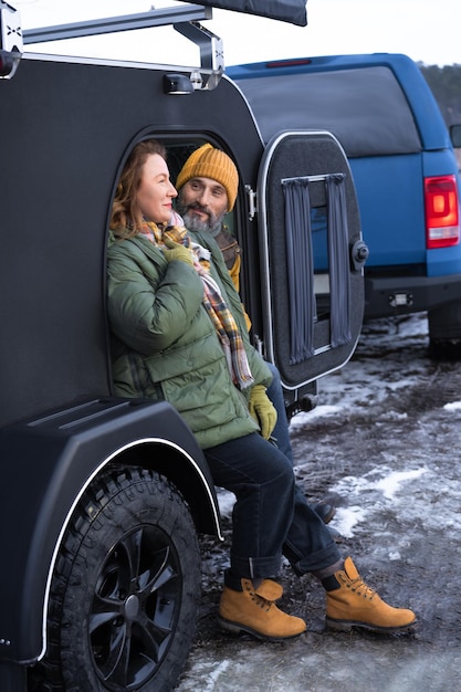 Pareja de mediana edad descansa en camper sonríe de buen humor en las vacaciones de invierno en la naturaleza Viajando por el país pareja madura descansa en camper mujer mira con amor a su esposo Concepto de viaje