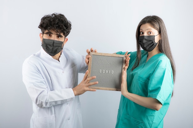 Pareja de médicos en uniformes sosteniendo un marco y mirando a cámara.