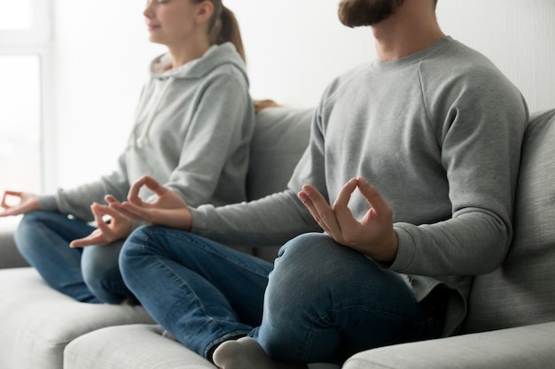 Pareja meditando practicando yoga en casa sofá, se centran en las manos