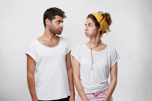 Pareja mirando ofensivo el uno al otro soplando sus mejillas después de discutir. hombre de moda con peinado de moda mirando con insulto a su esposa