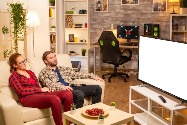 Pareja mirando la pantalla de TV blanco aislado a altas horas de la noche en la sala de estar.