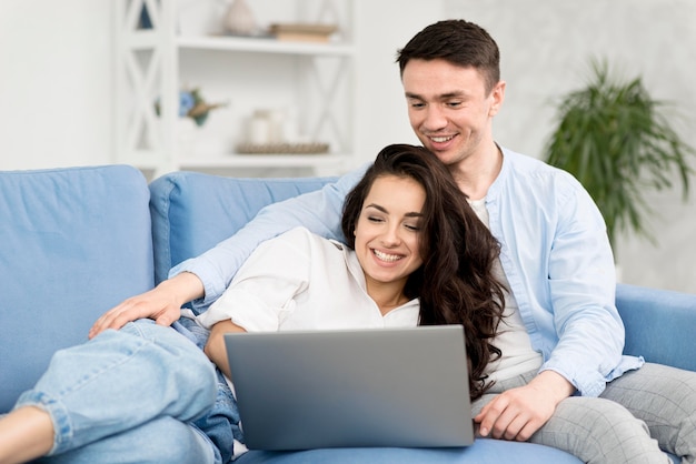 Pareja mirando portátil en casa en el sofá