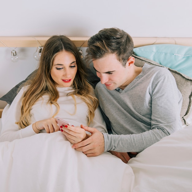 Foto gratuita pareja mirando smarthone en la cama