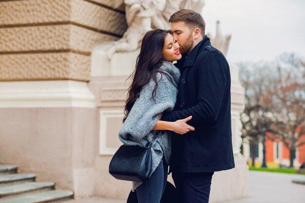 Pareja de moda joven posando en la calle vieja en otoño soleado. Mujer muy hermosa y su guapo novio elegante abrazando en la calle.