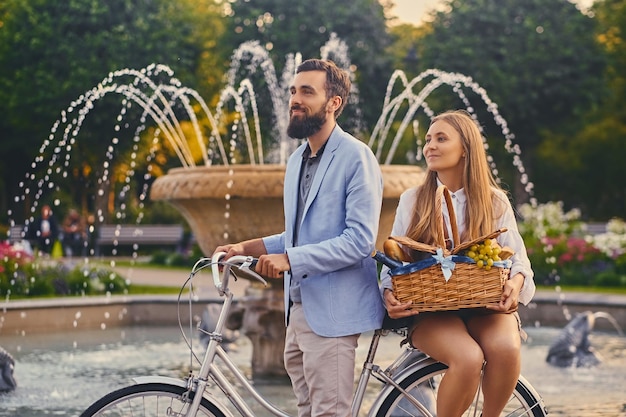 Pareja moderna con cesta de picnic sobre el fondo de la fuente de la ciudad.