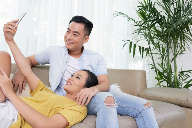 Pareja moderna tomando selfie en sofá en casa