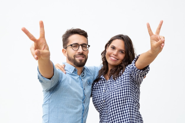 Foto gratuita pareja mostrando el signo de la victoria y sonriendo a la cámara