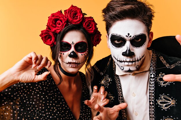 Pareja muerta espeluznante posando en la pared amarilla. chicos increíbles en traje de zombie celebrando Halloween.