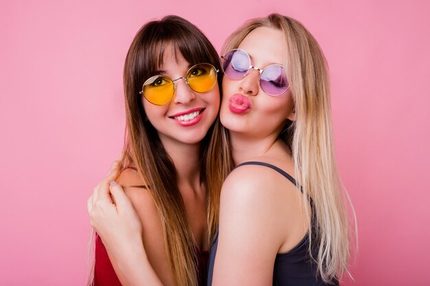 Pareja de mujeres sonrientes enviando beso y posando en la pared rosa