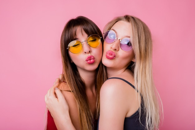 Pareja de mujeres sonrientes enviando besos y posando en pared rosa