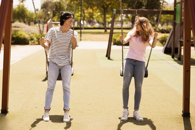 Pareja multiétnica de adolescentes columpiándose en el patio de recreo