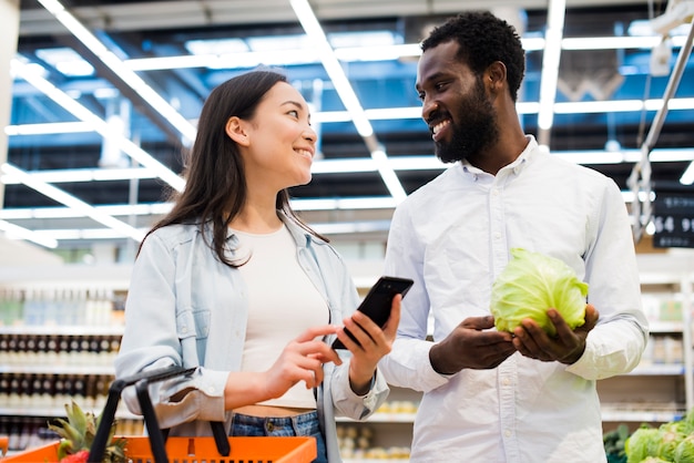 Pareja multirracial feliz eligiendo productos y mirando el uno al otro en el supermercado