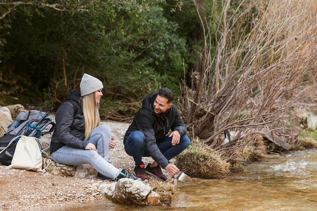 Foto gratuita pareja en la naturaleza bebiendo agua del río