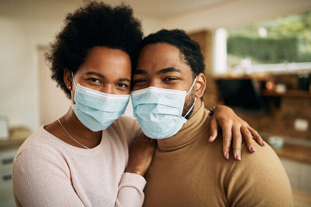 Pareja negra abrazada con máscaras protectoras en casa