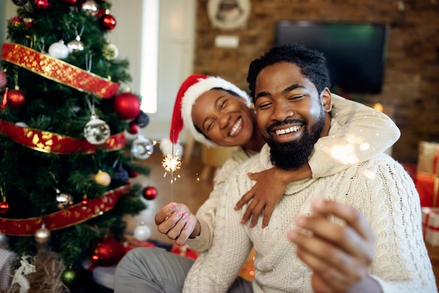 Pareja negra despreocupada divirtiéndose con bengalas el día de Navidad en casa