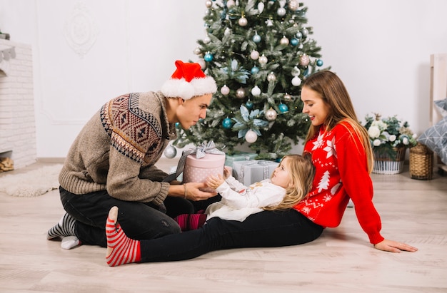 Pareja con niña enfrente de árbol de navidad