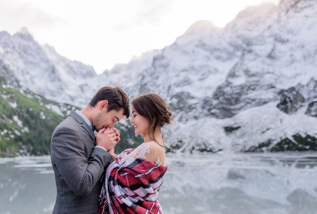 La pareja de novios se está calentando juntos en las montañas de invierno frente al lago congelado