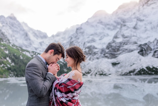 La pareja de novios se está calentando juntos en las montañas de invierno frente al lago congelado